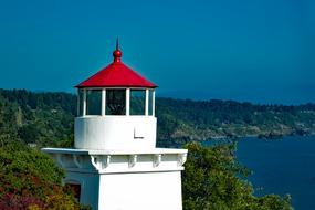 Beautiful, white and red Trinidad Memorial Lighthouse on the shore with colorful trees in California