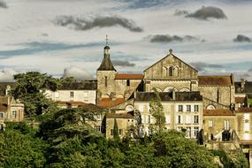 Beautiful Poitiers with church and other buildings, among the green plants, under the clouds in France
