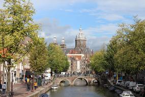 Beautiful river, with the bridge, among the colorful trees, people, cars and buildings, in Amsterdam, Netherlands