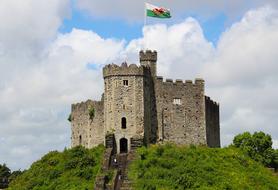 Beautiful castle with a flag of Wales, on the green hilltop, under cloudy sky