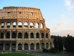 People, near the beautiful Colosseum, among the green trees, in Rome, Italy