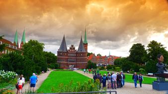 People, near the beautiful and colorful Holsten Gate, with the colorful garden in LÃ¼beck, Germany, under the colorful sky with the clouds