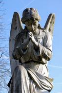 Shiny sculpture of the angel in sunlight, near the trees, under the blue sky