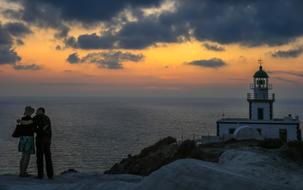 People, on the beautiful coastline of Santorini, Greece, with the lighthouse, at colorful and beautiful sunset, among the clouds