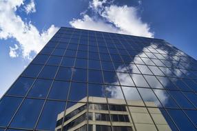 Low angle shot of the shiny, glass building with reflection of the other building, under the blue sky with clouds