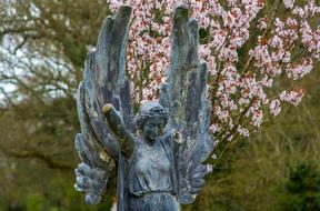 Beautiful statue of the angel, among the colorful plants, near the flowers