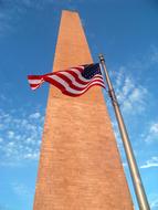 Colorful USA flag near the monument in Washington, USA, under the blue sky with white clouds