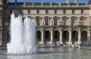 People near the beautiful fountain in sunlight, in Aile Richelieu, Louvre, Paris, France, under the blue sky