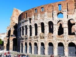 People near the beautiful, old Colosseum in sunlight, in Rome, Italy, under the blue sky