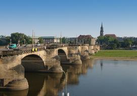 Beautiful city view with bridge above the river, near the colorful buildings and plants, under the blue sky