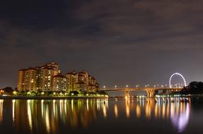 Landscape with the building near the bridge, at background with Ferris Wheel, with colorful lights, in Singapore, at the night