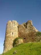 Beautiful ruin of the castle, among the green grass, under the blue sky