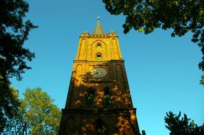 Beautiful and colorful church, among the green trees, in sunlight and shadows, under the blue sky