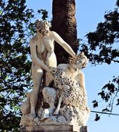 Sculpture with the people in sunlight, among the green trees, in Greece, under the blue sky