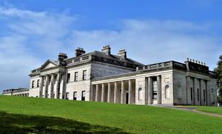 Beautiful castle with columns in sunlight, among the green grass, under the blue sky with clouds