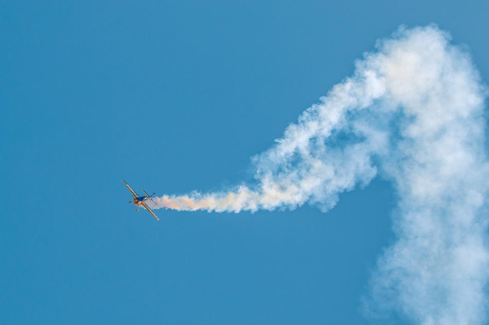 Colorful, flying Extra 300 aircraft with white contrail, at beautiful ...