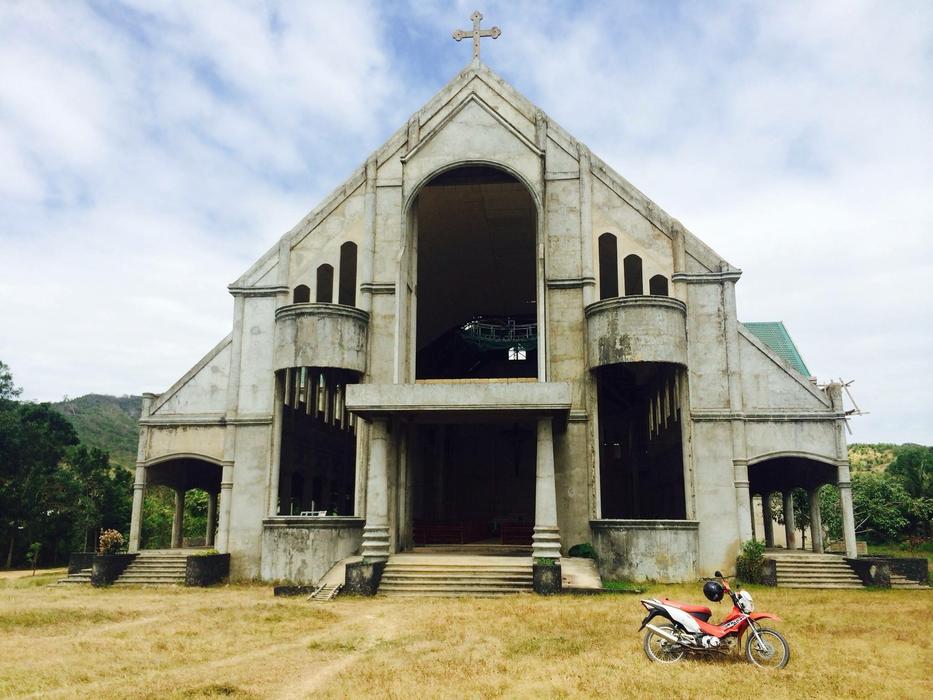 Motorbike, near the beautiful church with cross, on the yellow field, among the green trees in Manila, Philippines