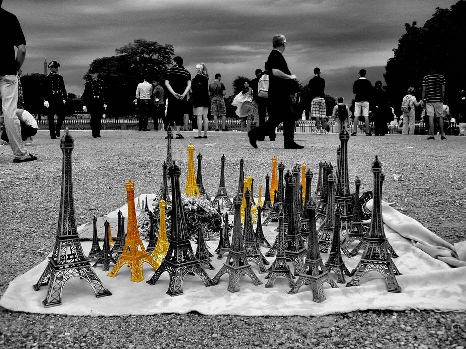Colorful figures of Eiffel Tower, on the cloth on the ground, among the people in black and white colors
