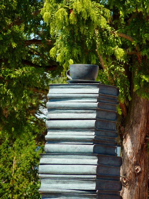 Sculpture of the books in sunlight, among the beautiful and colorful plants