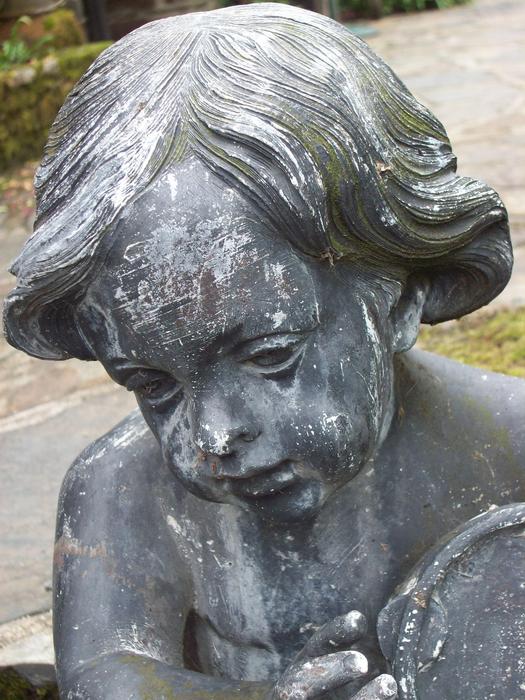 Beautiful sculpture of boy, among the colorful plants in the garden