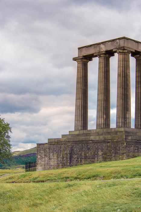 Beautiful National Monument of Scotland with columns, among the colorful plants, in Edinburg, Scotland, under the clouds