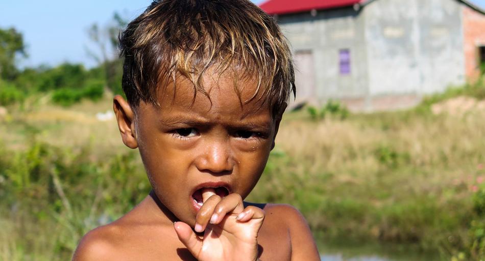 Portrait of the child boy with wet hair, near the Angkor Temple in Cambodia, among the colorful plants