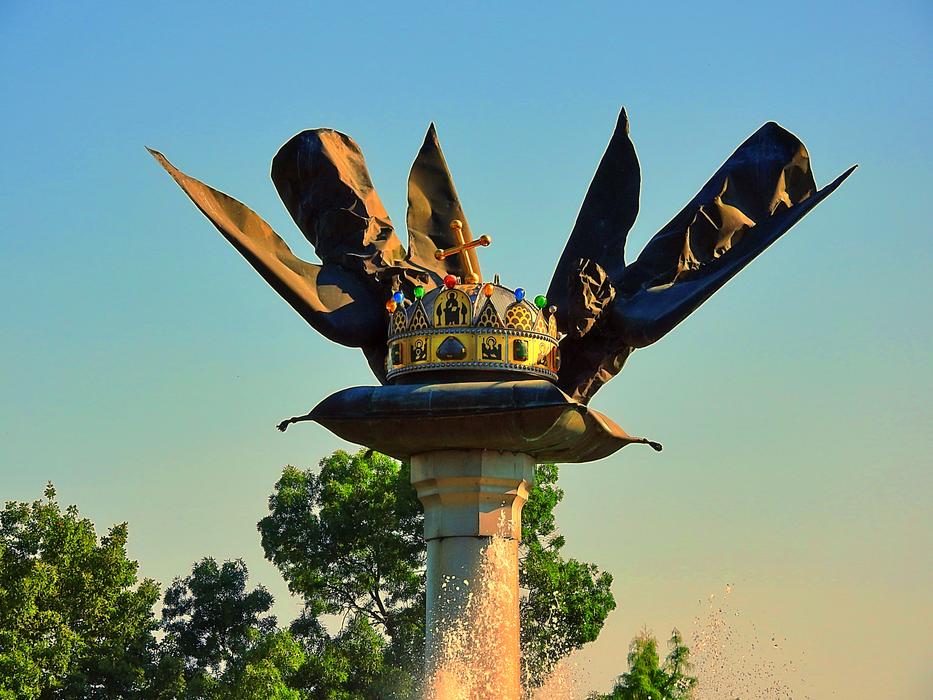 Shiny Royal Crown monument in Szarvas, Hungary, near the green trees, at colorful and beautiful, gradient sunset