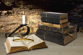 glasses on a bible, a stack of religious books and a candle in a candlestick on a table