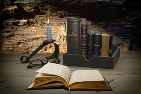 open bible, a stack of religious books and a candle in a candlestick on a table
