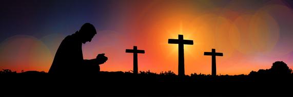 praying man near the crosses on the background of sunset