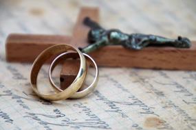 gold wedding rings on wooden cross with crucifix in blurred background