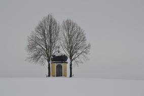 small chapel beneath two bare trees at snowy winter, austria, innviertel