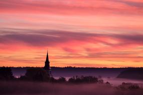 Beautiful, foggy landscape with the church in the village, at colorful and beautiful sunrise, in the clouds