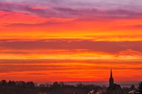 panorama of the city and the church steeple against the backdrop of a striped orange sunset