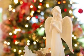 Beautiful, white angel statue, among the colorful and beautiful Christmas decorations on the Christmas tree