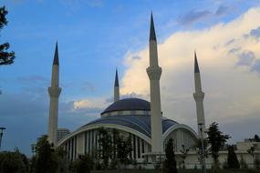 Beautiful cami with the minarets, among the plants, under the blue sky with clouds