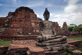 Beautiful statue of Buddha, near the temple, among the green plants, under the blue sky with clouds