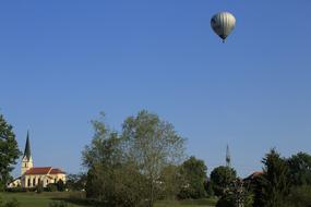 hot air balloon flies over trees and church