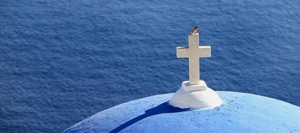 Colorful bird on the beautiful, white cross on the blue church in Santorini, Greece