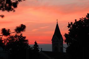 Beautiful steeple of the church, among the trees, at colorful and beautiful sunset in the sky, in the evening