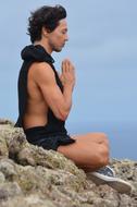 young man meditates on a rock by the sea