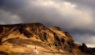 Landscape with the beautiful, white and red church on the yellow mountains, at cloudy sky, in Iceland