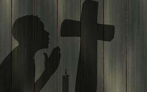 Black silhouette of a person, praying near the cross and candle, on the wooden wall