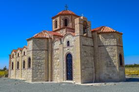 Beautiful, stone church with the roof, among the colorful plants, at beautiful blue sky on background, in Perivolia, Cyprus, Greece