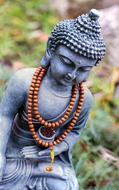 Beautiful statue of Buddha in meditation, with the praying beads, near the colorful plants