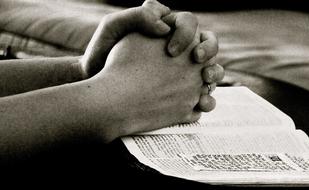 Black and white photo of the praying hands on the bible