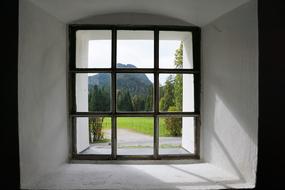 Beautiful view on the green mountains with the trees and Hintersteiner Lake, through the window in the white wall of the BÃ¤rnstatt Chapel in Scheffau, Austria