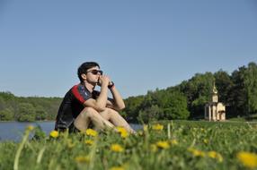 young man sits on a field of dandelions on the background of the church