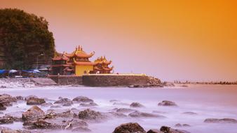 Beautiful and colorful temple on the shore, with the rocks and trees, at colorful and beautiful sunset