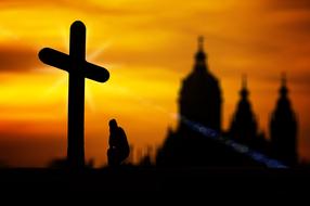 photo of a cross and a cathedral against the background of a golden sunset